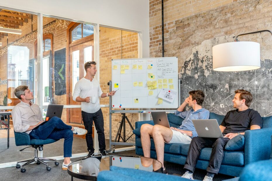 three men sitting while using laptops and watching man beside whiteboard